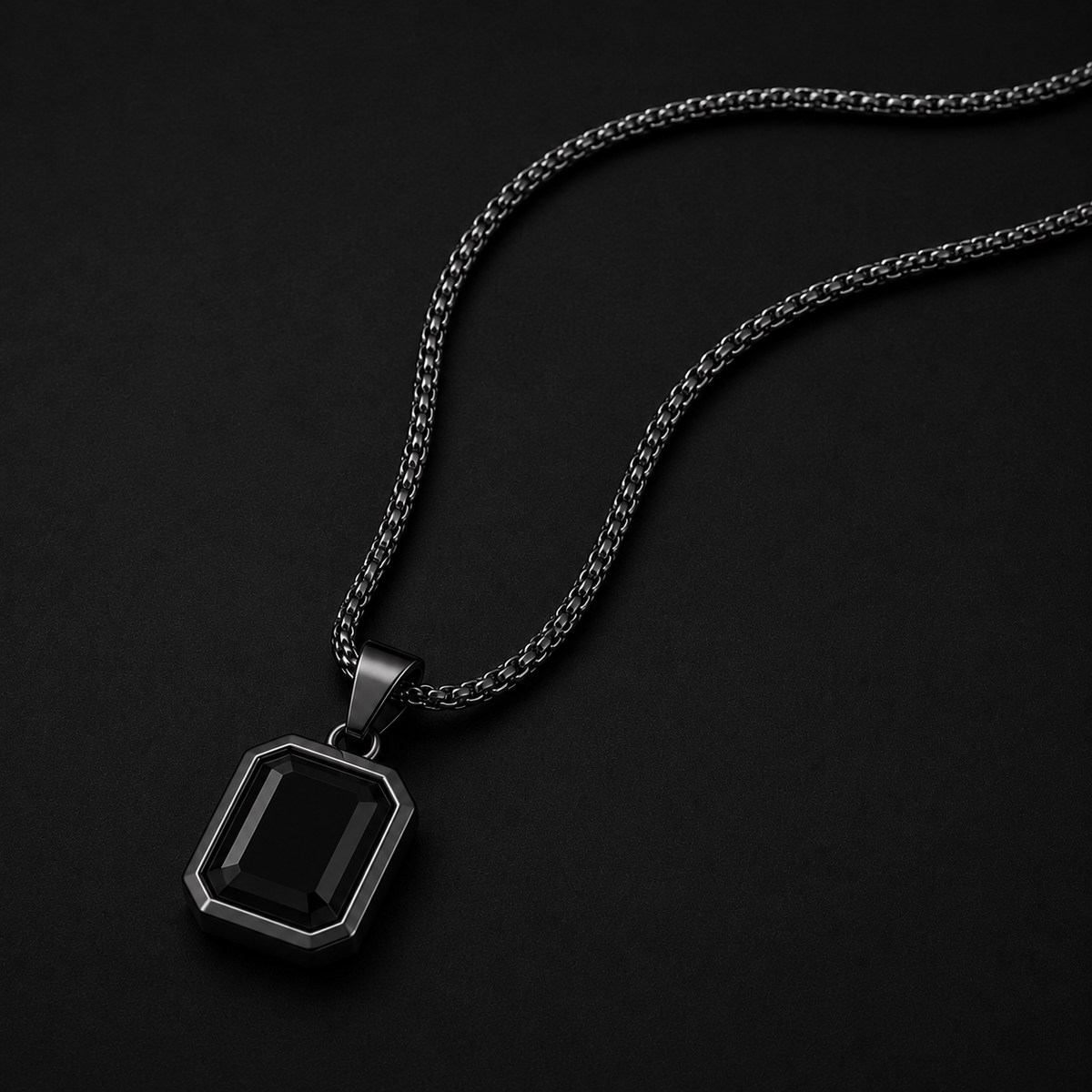 A men's pendant necklace featuring a rectangular faceted black gemstone in a dark gunmetal silver bezel, suspended from a matching dark silver chain against a solid black background.