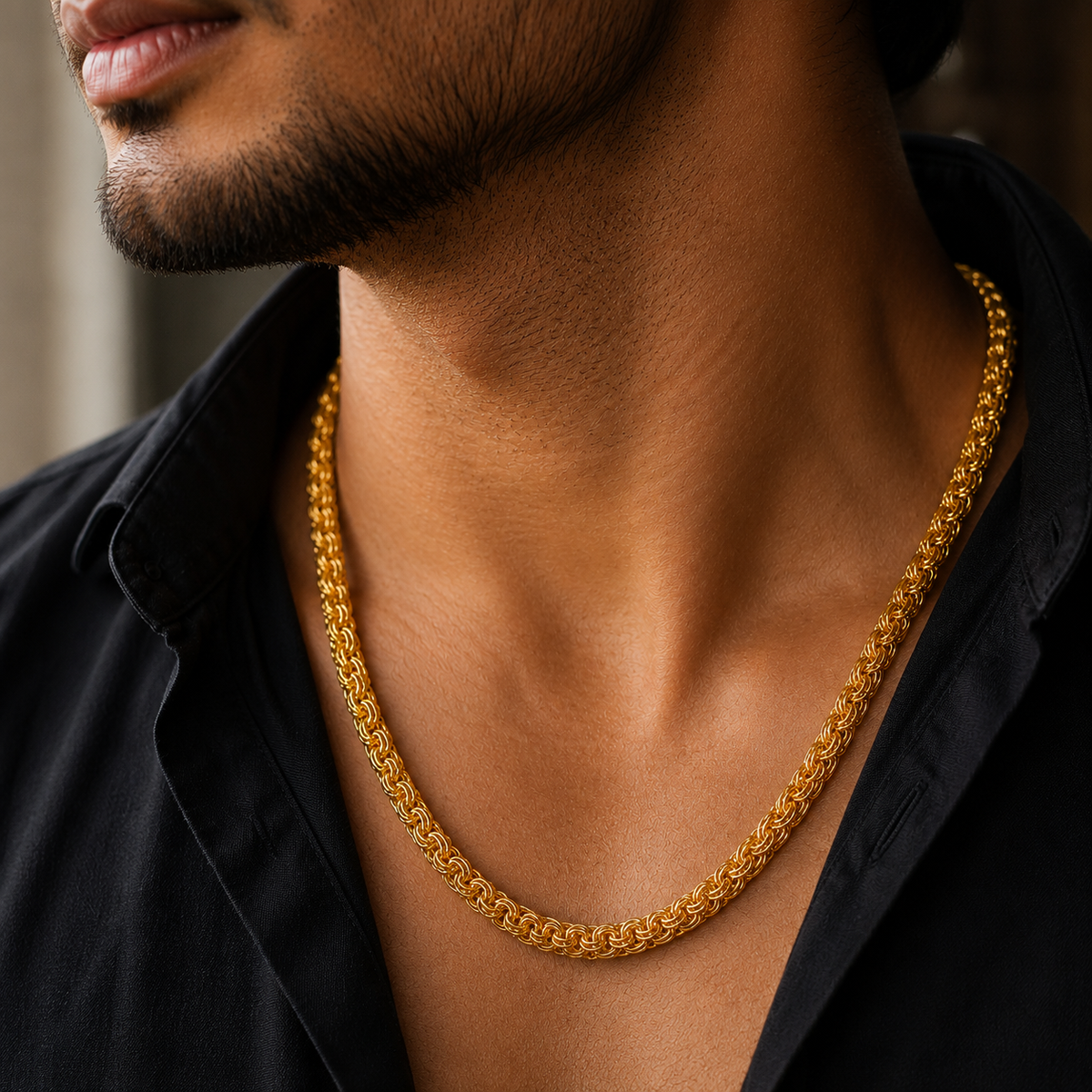 A close-up lifestyle shot of a man wearing a thick, textured gold chain necklace over a black collared shirt.