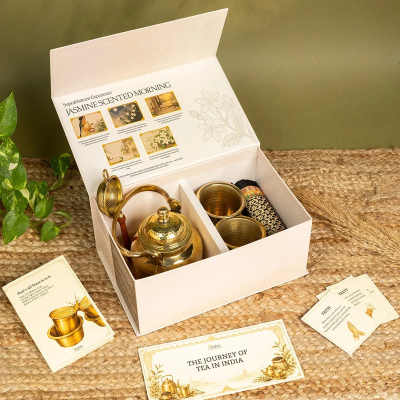 Open Suprabhatam gift box with brass tea kettle, tea strainer, two hammered tumblers and rolled Madur coaster, with Journey of Tea in India card. Zishta Diwali Gifts.
