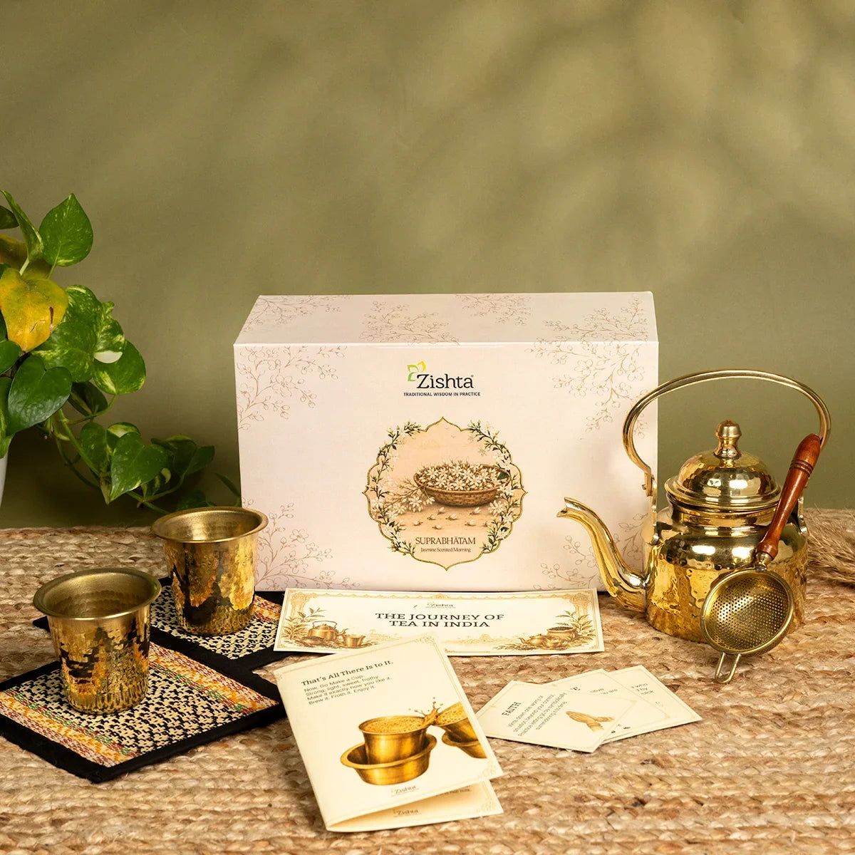 Hammered brass tea kettle, two brass tumblers on Madur coasters and brass tea strainer beside the Zishta Suprabhatam Jasmine Scented Morning box. Zishta Diwali Corporate Gifts.
