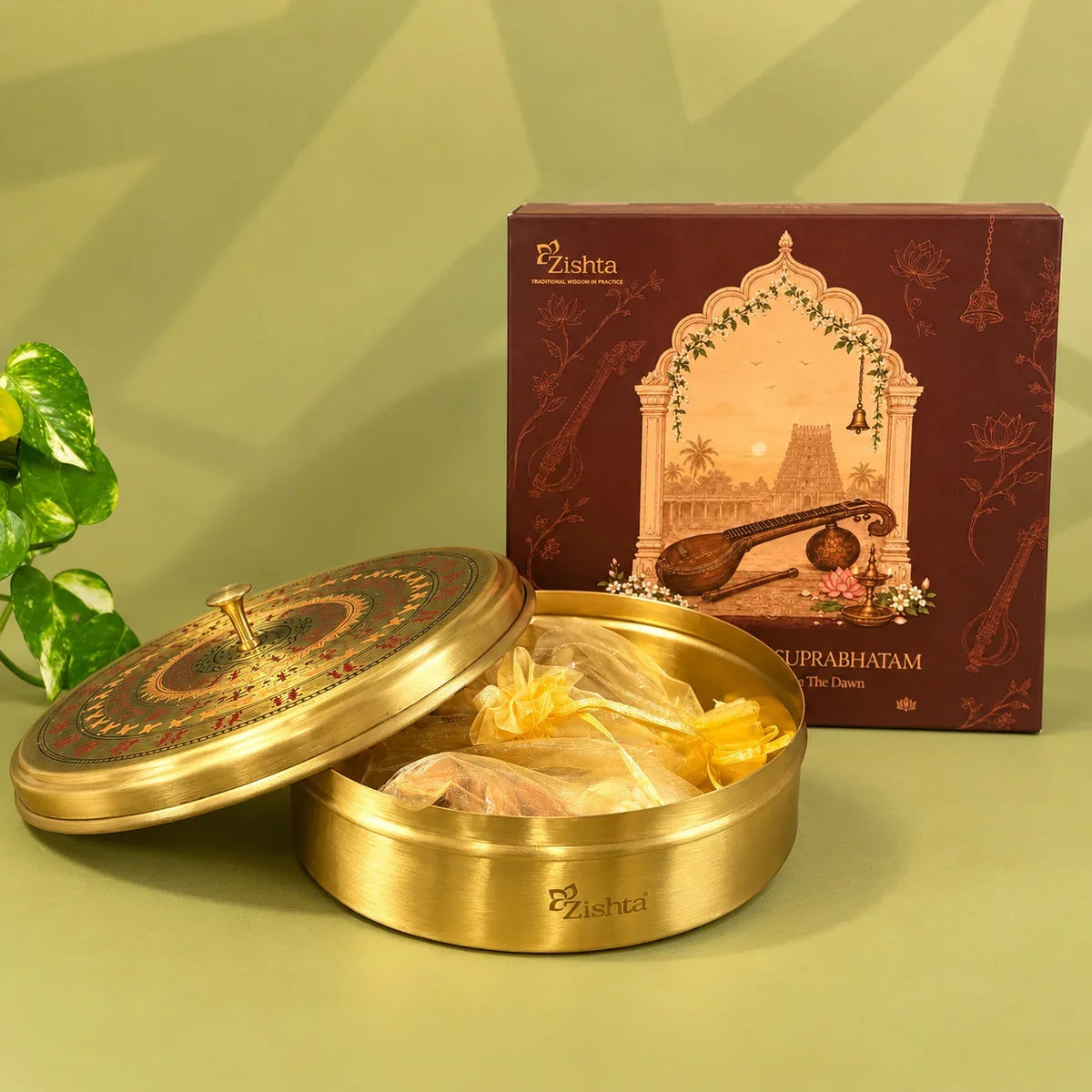 Open round brass Worli art box with gold organza dry fruit pouches inside, beside the Zishta Suprabhatam gift box.