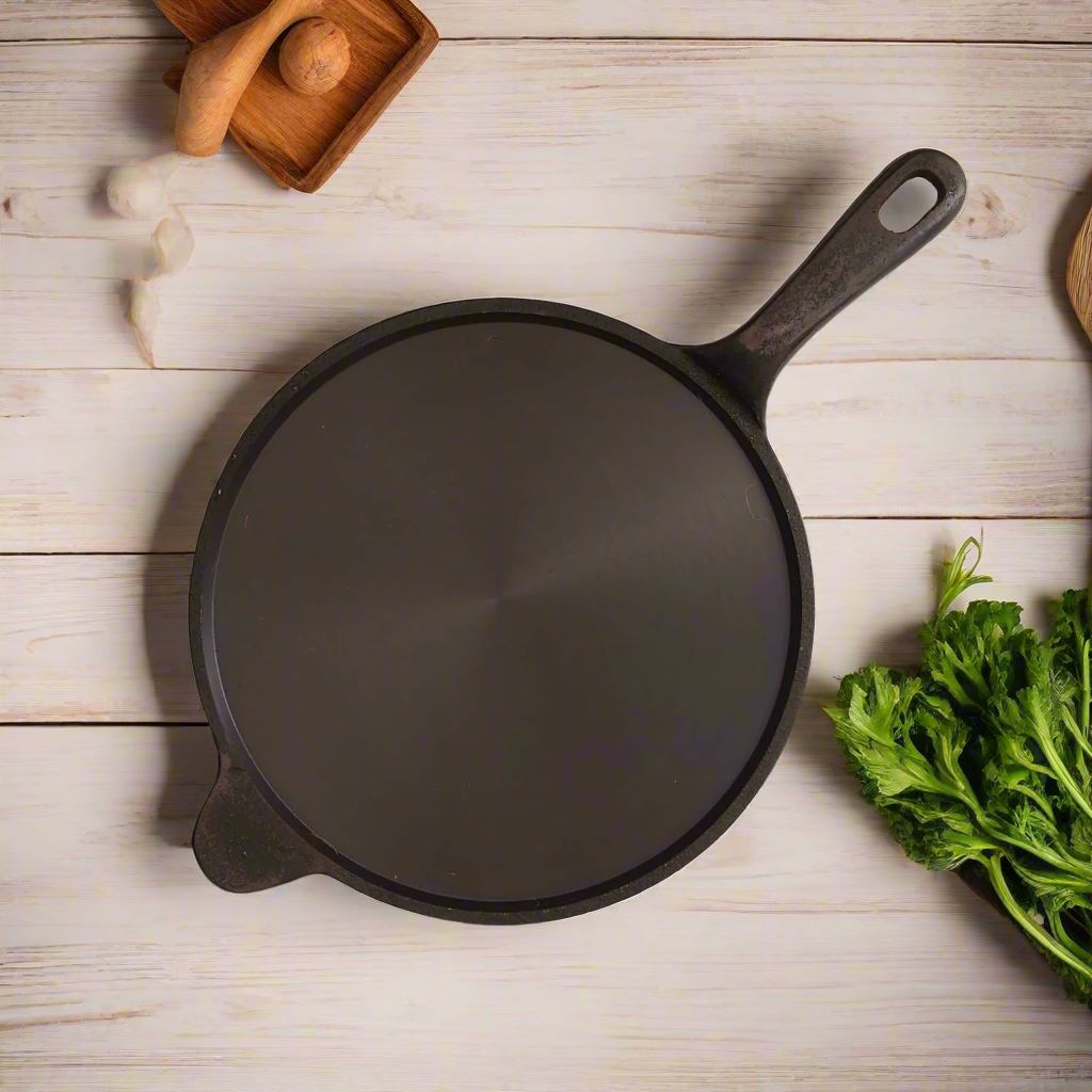 Black cast iron Tawa with a long handle on a wooden surface with green vegetables-Zishta Traditional Cookware
