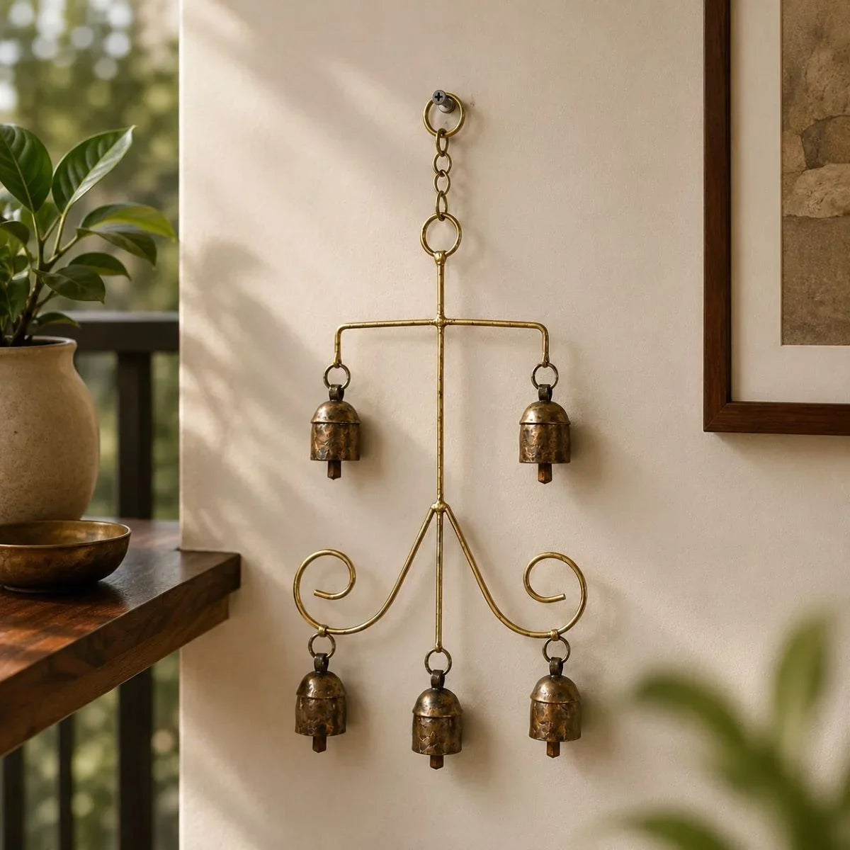 Copper coated iron wall hanging with five bells - Vriksha design near a plant in the balcony. Zishta Home Decor.