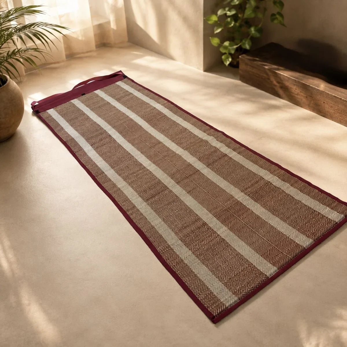Madur travel mat in maroon with carry strap laid out on a floor. ZIshta Home Decor.