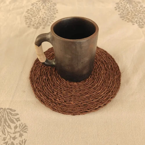 Manipur Black  Pottery Milk Cup on a brown woven coaster with a floral-patterned fabric background-Zishta Traditional Serveware