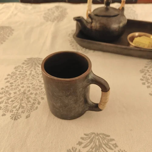 Manipur Black  Pottery Milk Cup on a patterned tablecloth with a teapot in the background-Zishta Traditional Serveware