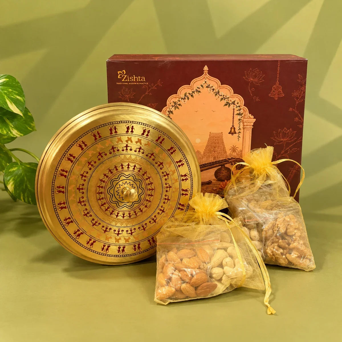Full view of a brass box lid with red and orange Warli tribal figures in circles, with dry fruit pouches and the Zishta gift box